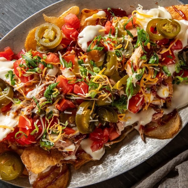 Close-up of BBQ nachos with pulled pork, melted cheese, jalapeños, tomatoes, and green onions.